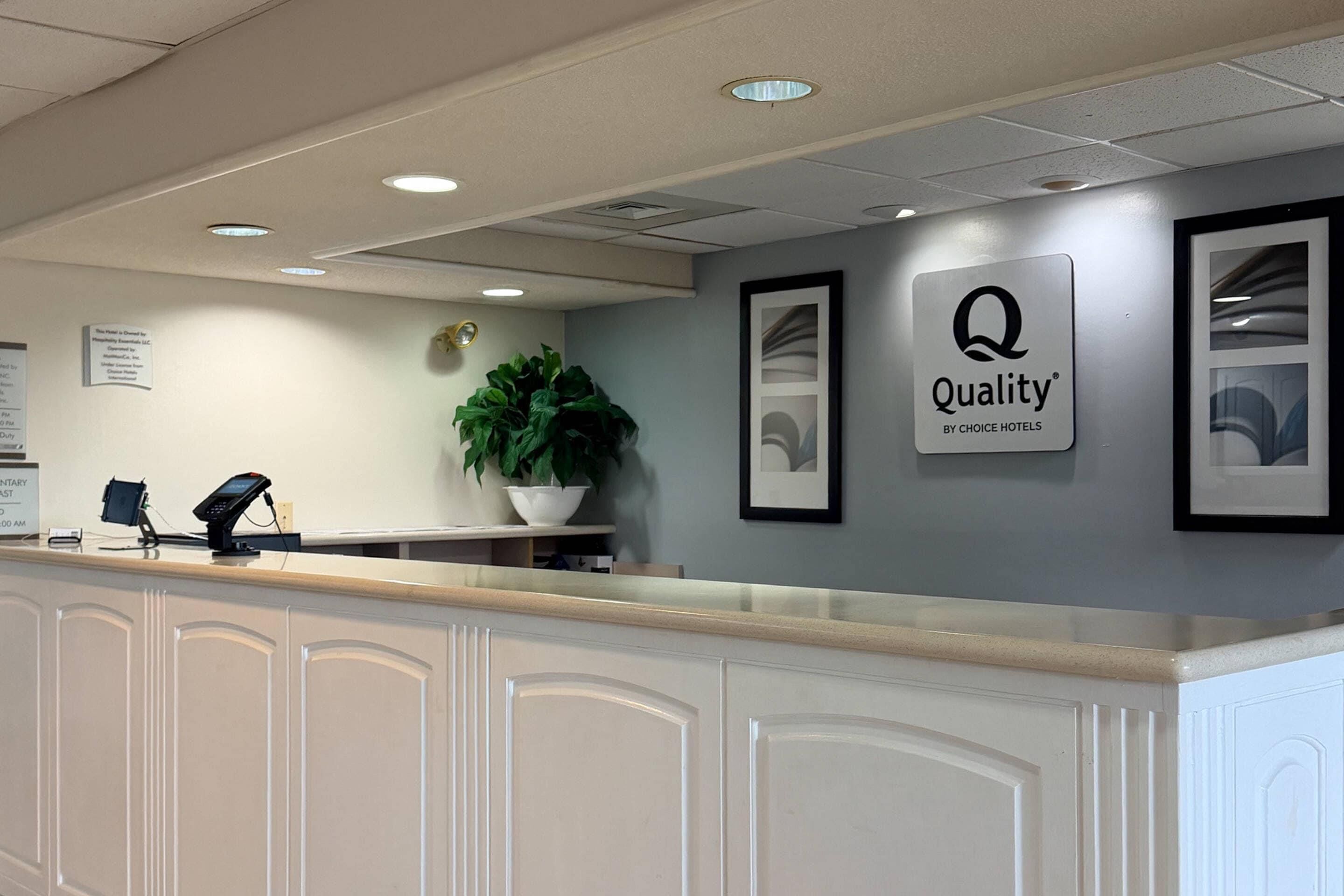 A hotel reception area with a reception desk, a potted plant, and framed pictures on the wall.