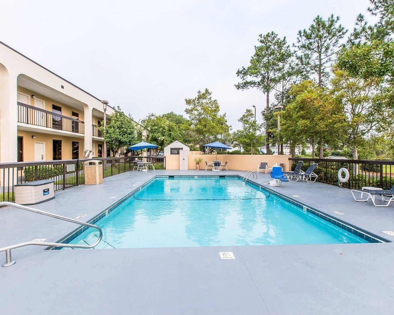 A swimming pool with lounge chairs and umbrellas, surrounded by a building with balconies.