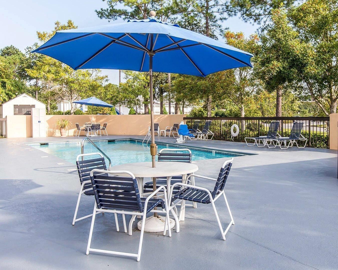 A poolside area with a table and chairs, a pool, and umbrellas.
