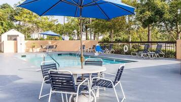 A poolside area with a table and chairs, a pool, and umbrellas.