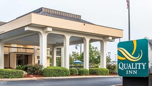 Ein Hotel mit überdachter Eingangspartie, einem Schild für Quality Inn und einer Fahnenstange mit der US-amerikanischen Flagge.