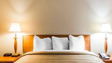 A hotel room with a bed, two bedside lamps, a nightstand with a phone, and a wall clock.