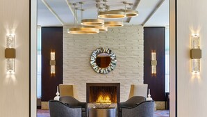 A lobby with a fireplace, two armchairs, and a round mirror on a brick wall. - Hilton Los Angeles North/Glendale (Glendale)