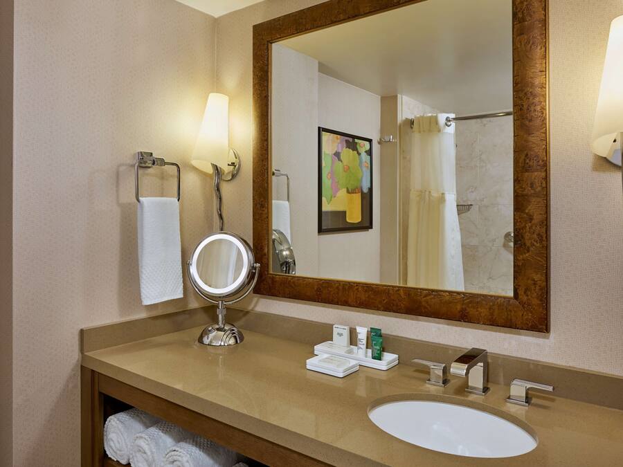Bany d'hotel amb un mirall gran, un lavabo, un penjador de tovalloles i dues làmpades fixades a la paret.
