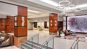 A modern lobby with a reception desk, seating area, and a large abstract wall art piece. - Hilton Los Angeles North/Glendale (Glendale)