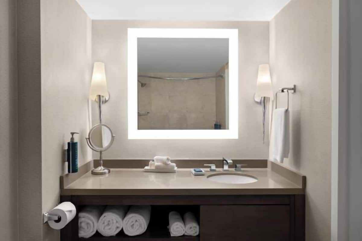 Een moderne badkamer met een grote spiegel, een wastafel, een handdoekhouder en een toiletrolhouder.