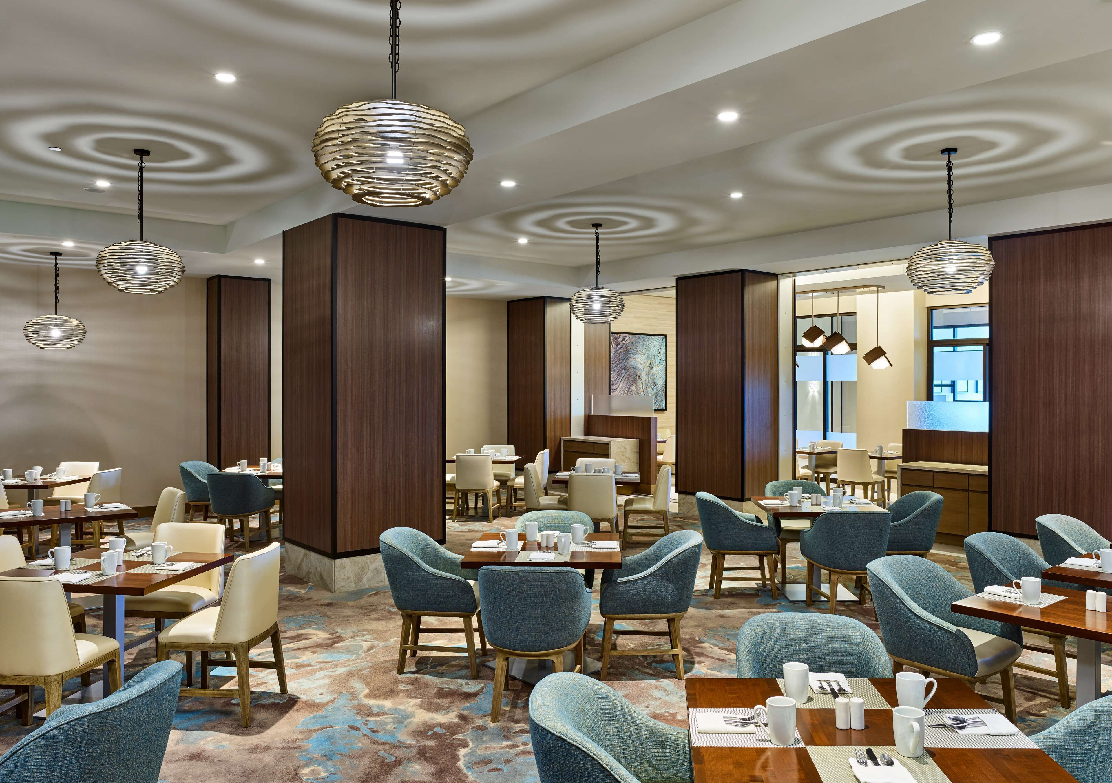 A hotel dining area with round tables, blue upholstered chairs, and pendant lighting.