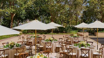 An outdoor dining area with round tables, chairs, and white umbrellas.