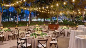 An outdoor dining area with round tables, chairs, and string lights. - Hilton Los Angeles North/Glendale (Glendale)