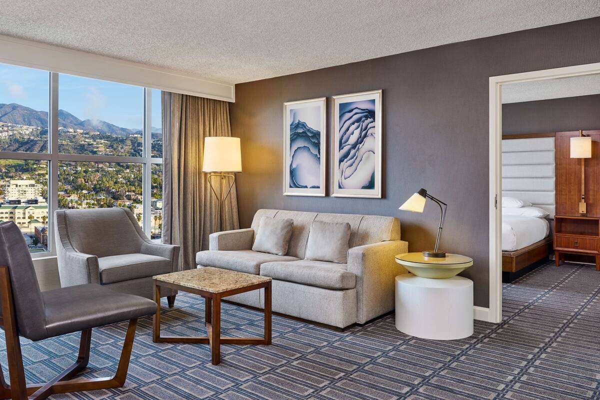 Een hotelkamer met een groot raam, een bank, een stoel, een kleine tafel en een bed.