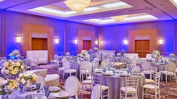 Un salón de banquetes con mesas redondas, sillas blancas y centros de mesa florales.