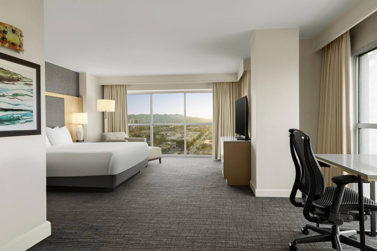 Een hotelkamer met een groot bed, een bureau met stoel, een televisie en uitzicht op de stad.
