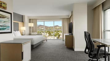 Ein Hotelzimmer mit Bett, Schreibtisch, Sessel, Fernseher und einem großen Fenster mit Bergblick.