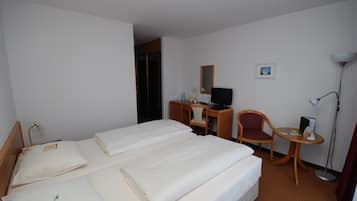 A hotel room with two beds, a desk, a chair, a desk lamp, and a small table.