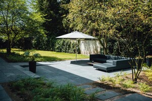 Ein Terrassenbereich im Freien mit moderner Sitzgruppe und einer Pergola, die Schatten spendet.