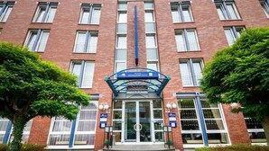 L’entrée d’un hôtel, avec une porte en verre, un auvent bleu et une enseigne indiquant qu’il s’agit de l’« hôtel Düsseldorf City ».