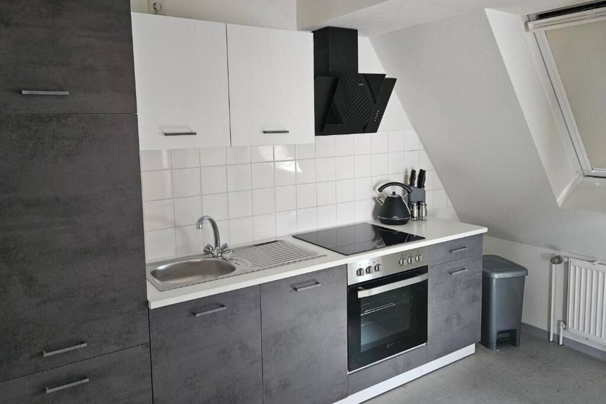 Een moderne keuken met grijze kastjes, een wit aanrecht, een inbouwoven en een raam boven de gootsteen.