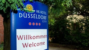 Un panneau bleu portant l’inscription « HK-Hotel DÜSSELDORF CITY » en blanc et « Willkommen Welcome » en rouge.