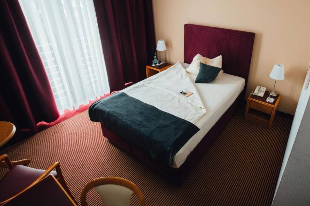 Een hotelkamer met een bed, twee nachtkastjes, een stoel en een raam met gordijnen.
