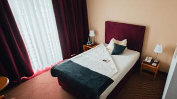 A hotel room with a bed, two bedside tables, a chair, and a window with curtains.