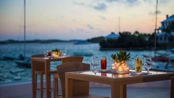 A dining table with chairs and a view of the sea at dusk.
