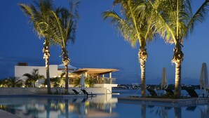 Un hôtel moderne doté d’une piscine, de palmiers et offrant une vue sur la ville au crépuscule.