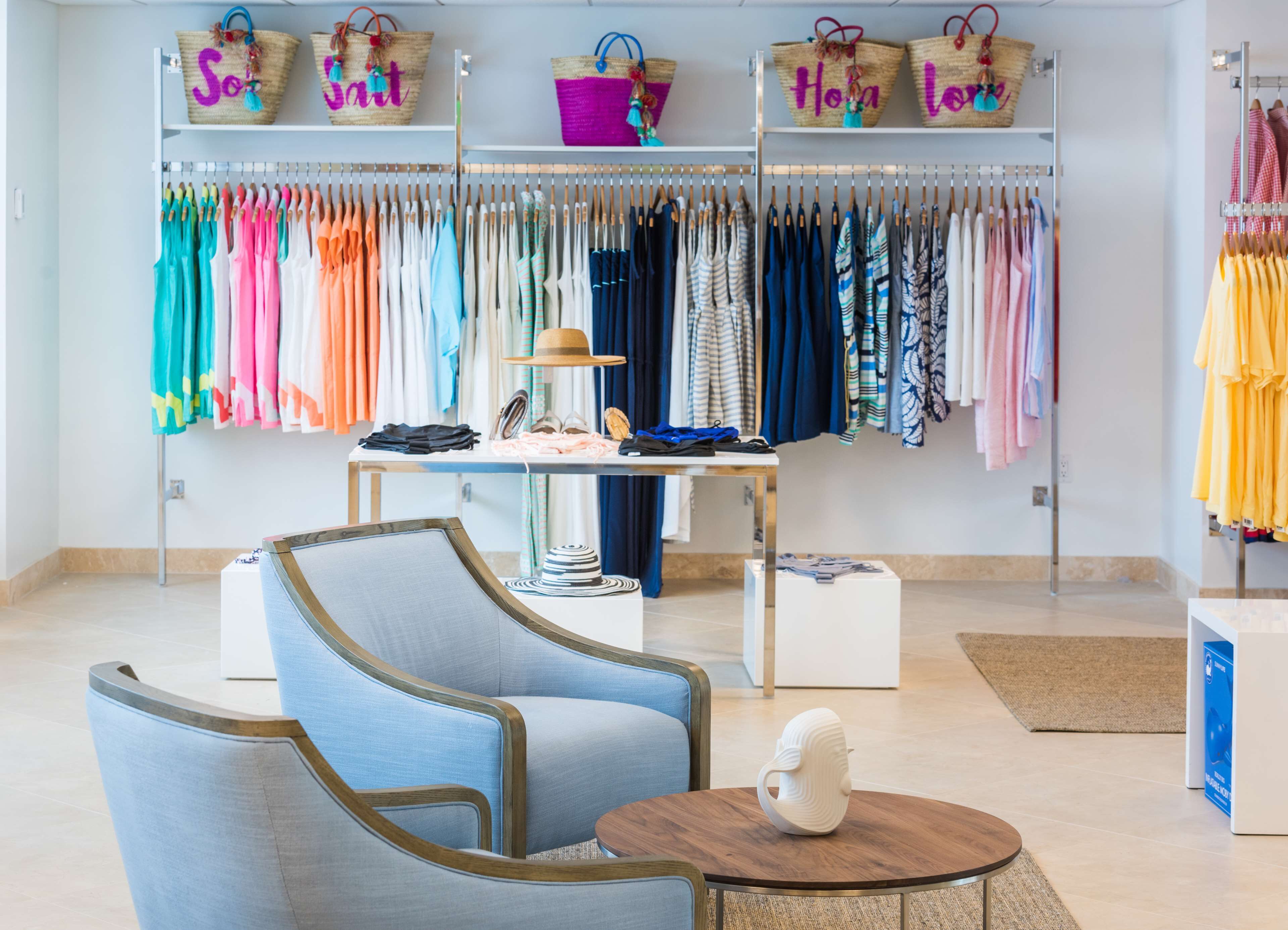 A boutique hotel room with a seating area, a table with a decorative item, and a clothing rack with various garments.