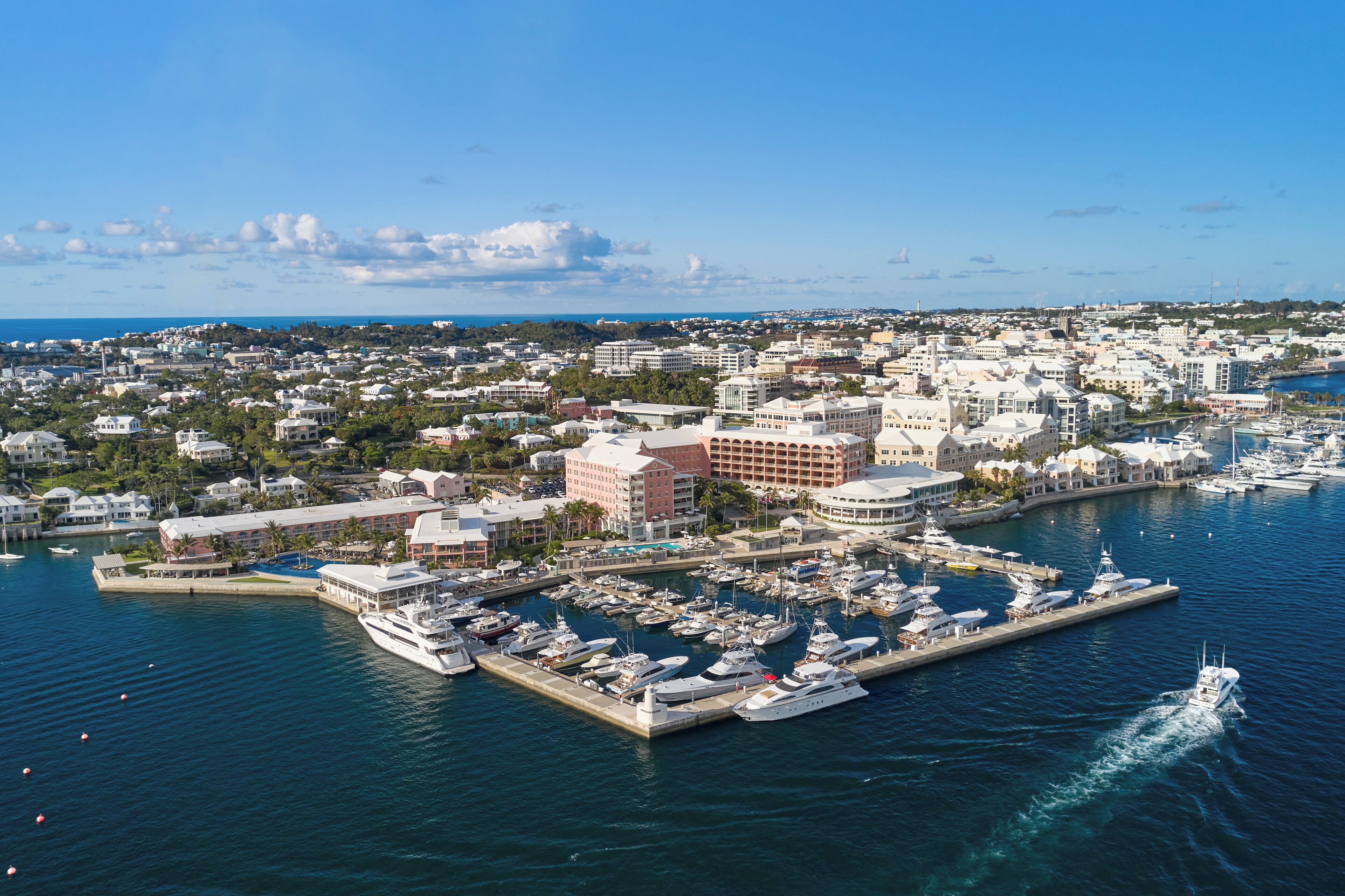 A marina with multiple boats docked, surrounded by buildings and a clear sky.