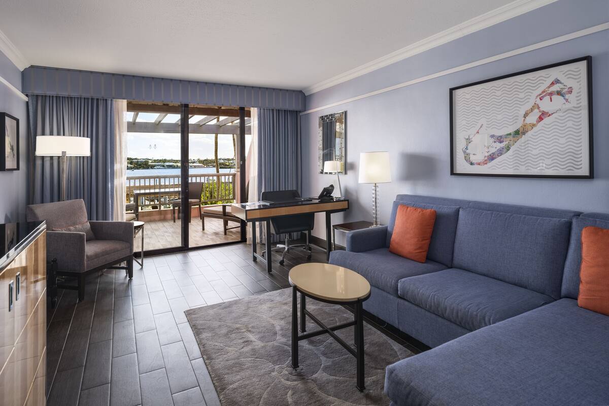 Ein modernes Hotelzimmer mit Balkon, einer Couch, einem Schreibtisch und einem Sessel.