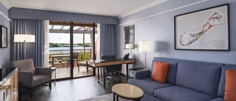 A modern hotel room with a balcony, a sofa, a desk, and a chair.