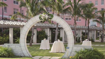 A pink building with a white archway leading to a garden area with tables and chairs.