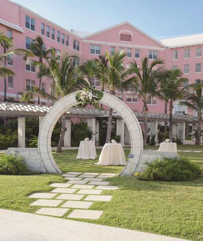 A pink building with a white archway leading to a garden area with tables and chairs.