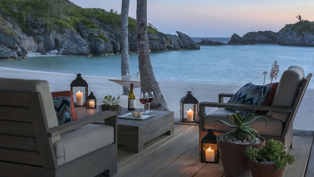 Un espace de détente aménagé au bord de la plage, avec une terrasse en bois, deux chaises longues, une petite table agrémentée d'une bougie, des verres à vin et des plantes en pot.