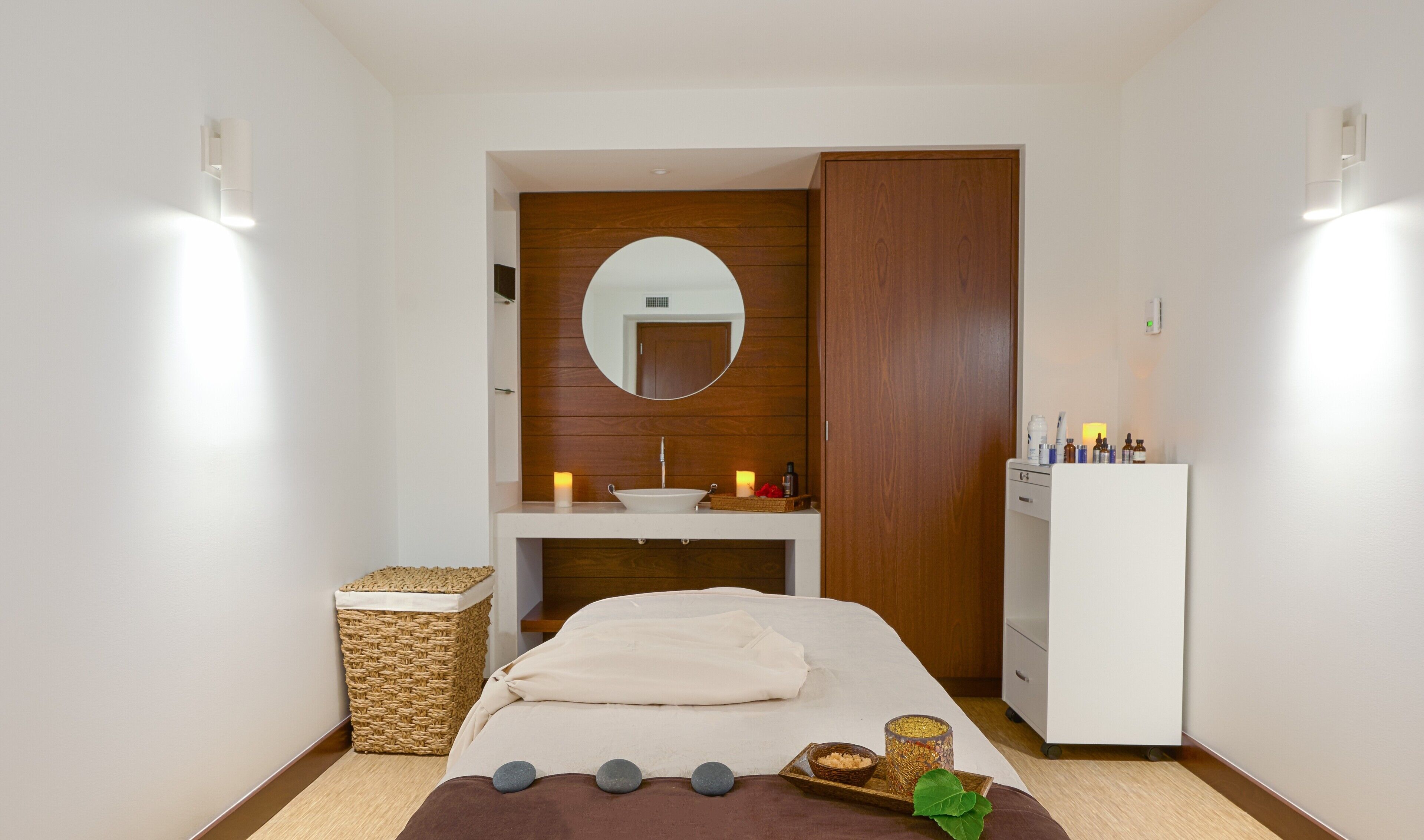 A spa room with a bed, a wooden vanity, a mirror, a white sink, and a small cabinet.