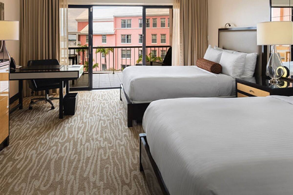 Ein Hotelzimmer mit zwei Betten, einem Schreibtisch, einem Fernseher und Blick auf Gebäude.
