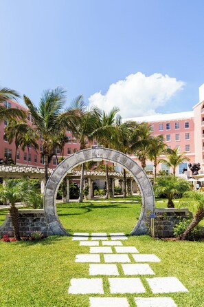 A courtyard with a stone archway, palm trees, and a building with pink and white exterior walls. - Hamilton Princess & Beach Club - A Fairmont Hotel (Pembroke Parish)