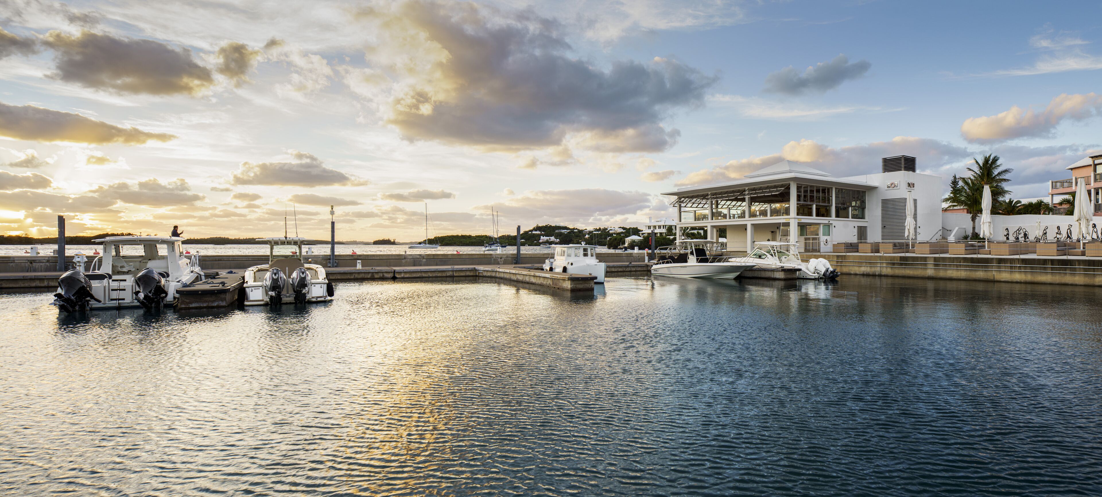 Un port de plaisance avec des bateaux amarrés, un bâtiment moderne doté de grandes fenêtres et une vue sur le front de mer.