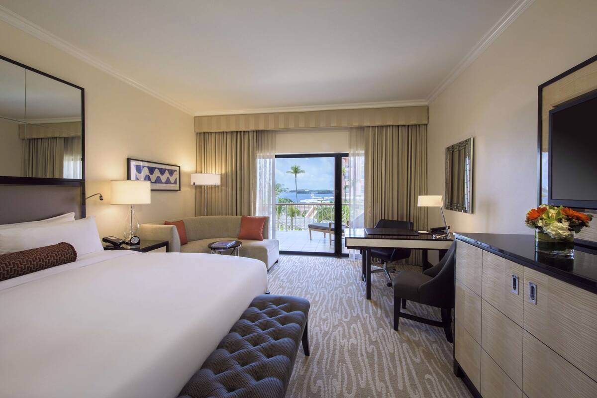 Ein Hotelzimmer mit einem großen Bett, einem Schreibtisch, einer Couch und Blick ins Freie.