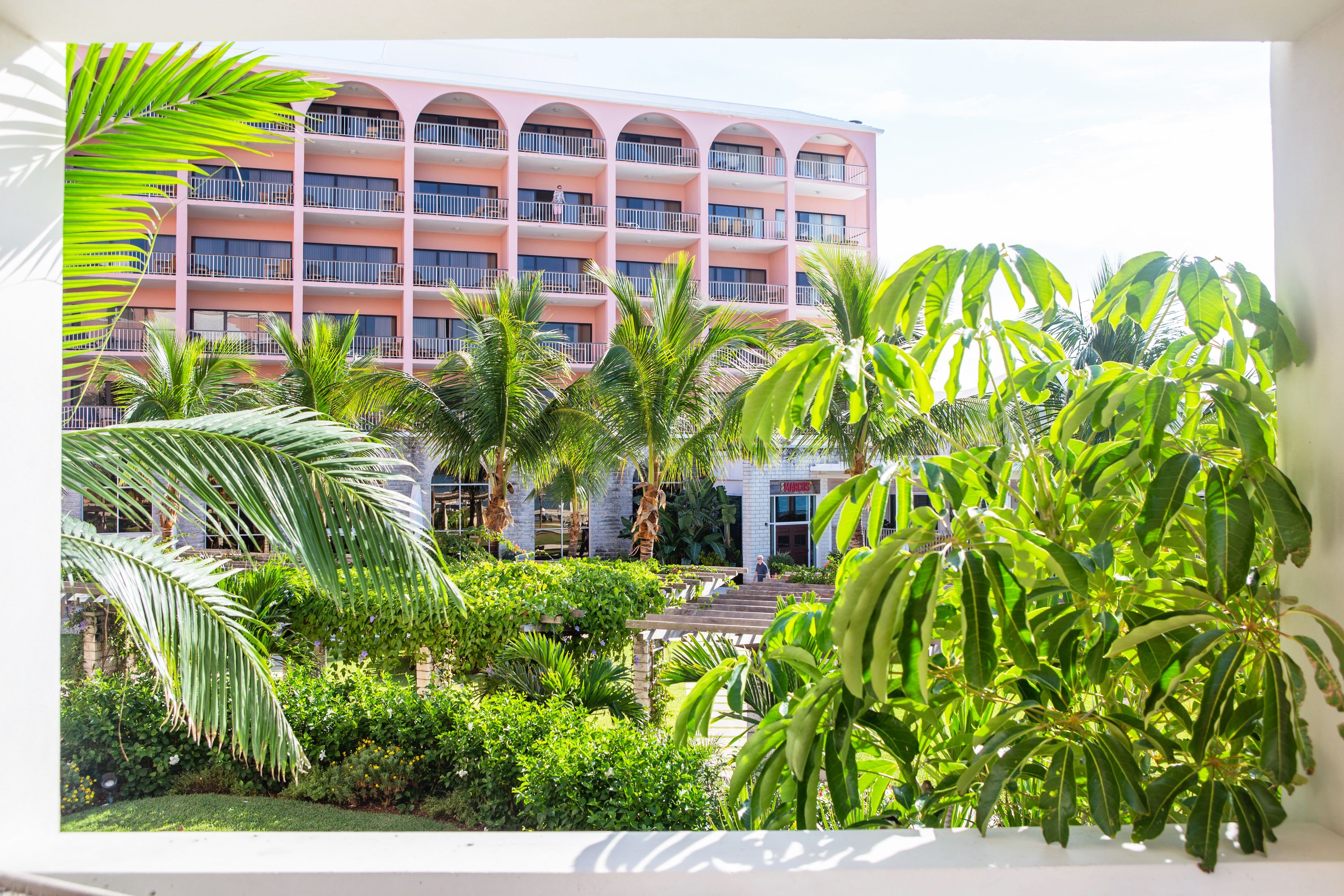 A multi-story hotel with balconies, surrounded by lush greenery and palm trees.