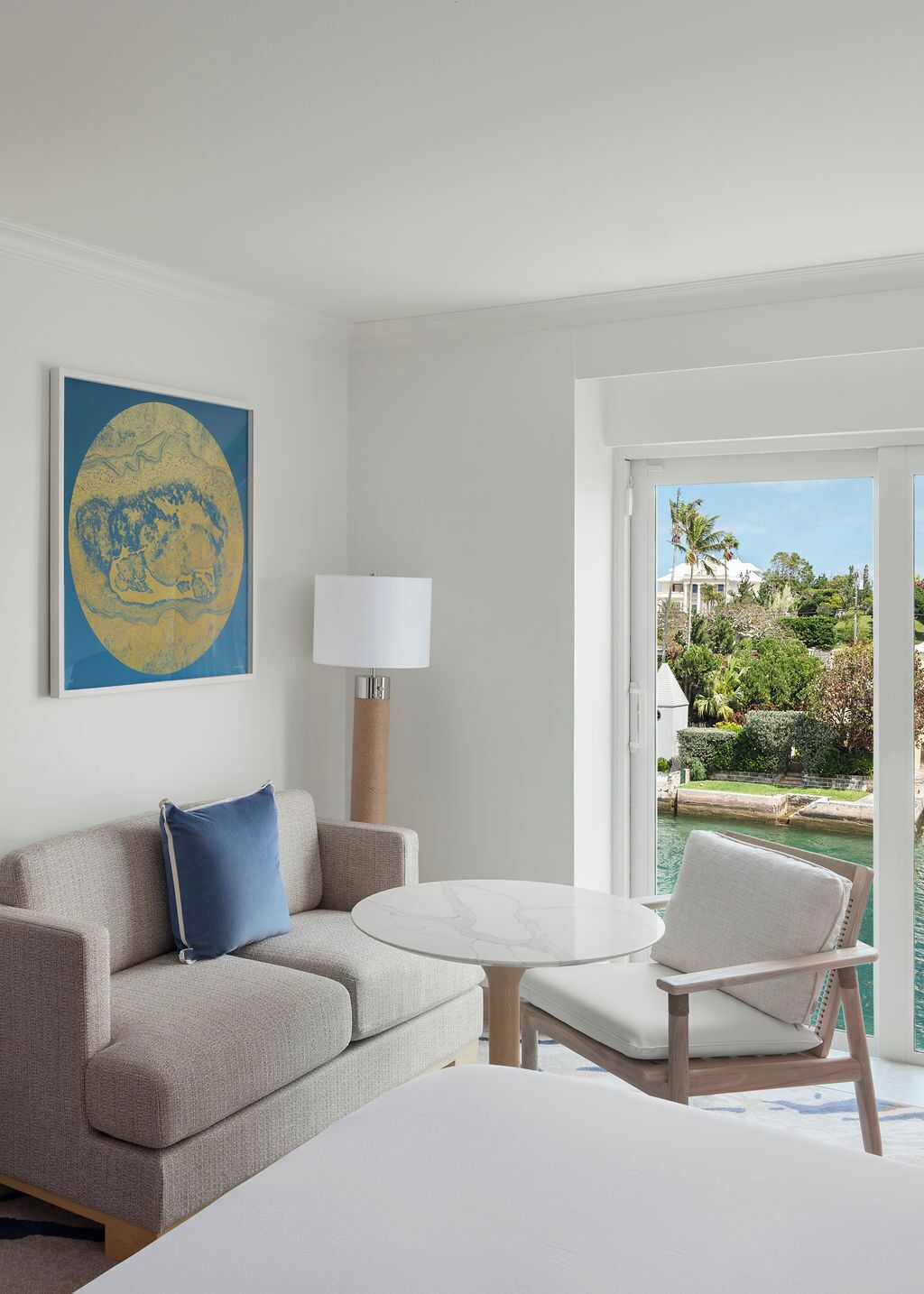 A hotel room with a sofa, a small table, a chair, a bed, a lamp, and a painting.
