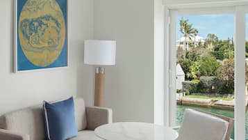 A hotel room with a sofa, a small table, a chair, a bed, a lamp, and a painting.
