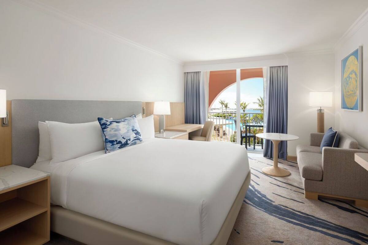 Ein Hotelzimmer mit einem großen Bett, einem Schreibtisch, einem Stuhl und Blick auf den Poolbereich.