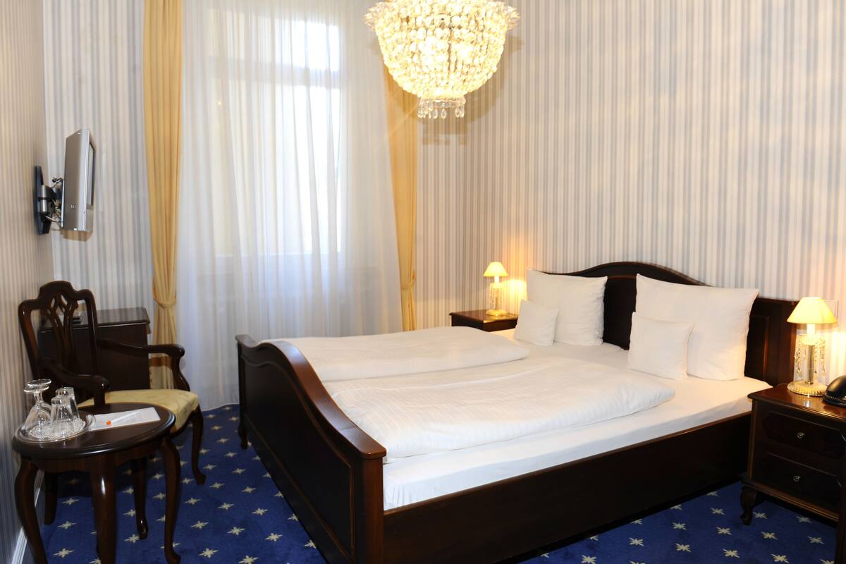 Habitación de hotel con una cama grande, un escritorio con silla, un candelabro y un televisor en la pared.