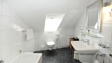 Un baño moderno con tragaluz, azulejos blancos, una bañera, un inodoro y un lavabo con espejo.