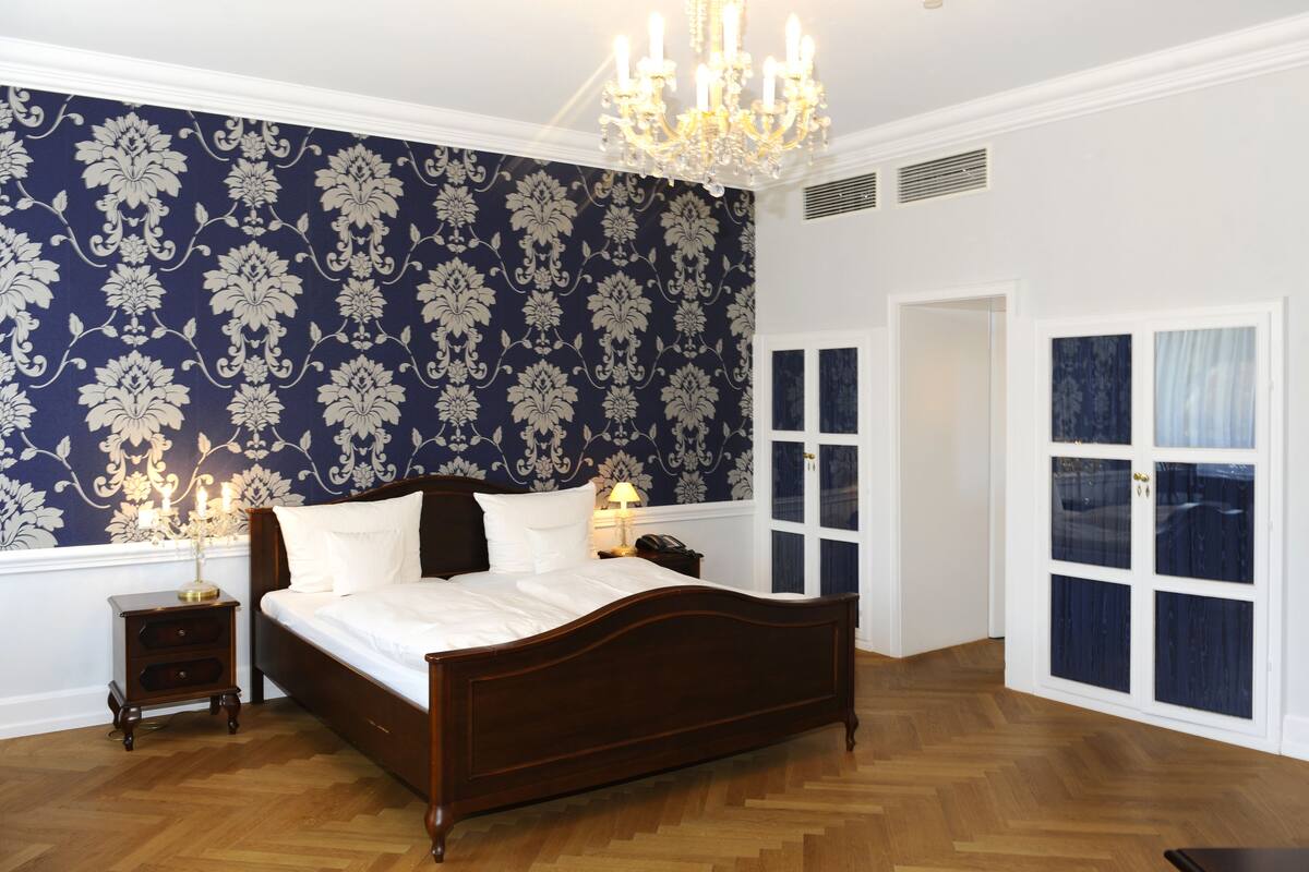 Un dormitorio con una cama grande, una araña, una mesita de noche y una puerta con paneles de vidrio.