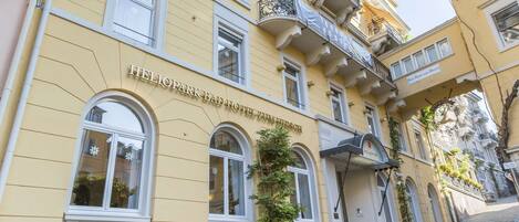 A yellow building with the sign "Heliopark Bad Hotel Hohenschönhausen" and a cobblestone street.