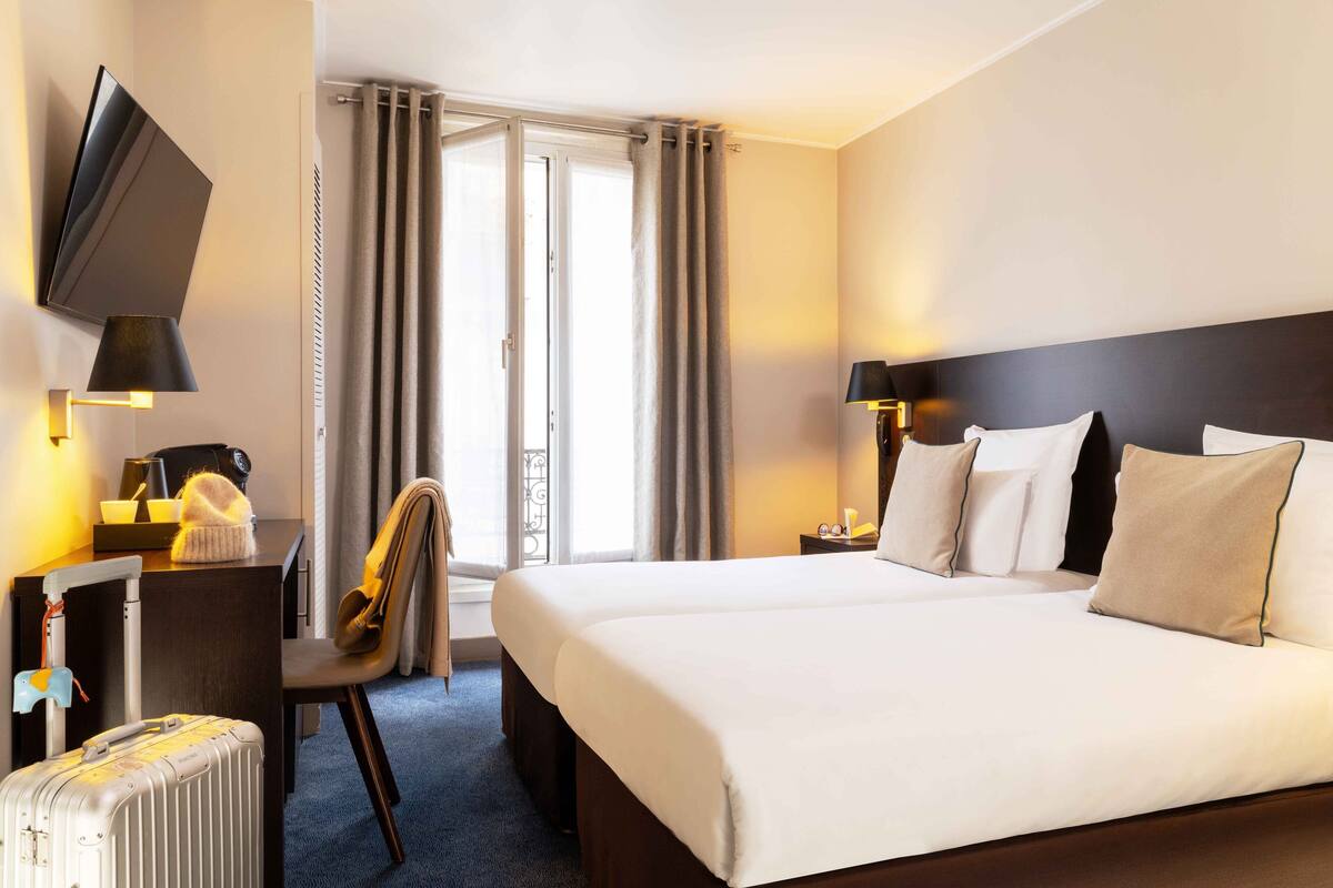 A hotel room with a large bed, a desk with a chair, a TV mounted on the wall, and a suitcase on the floor.