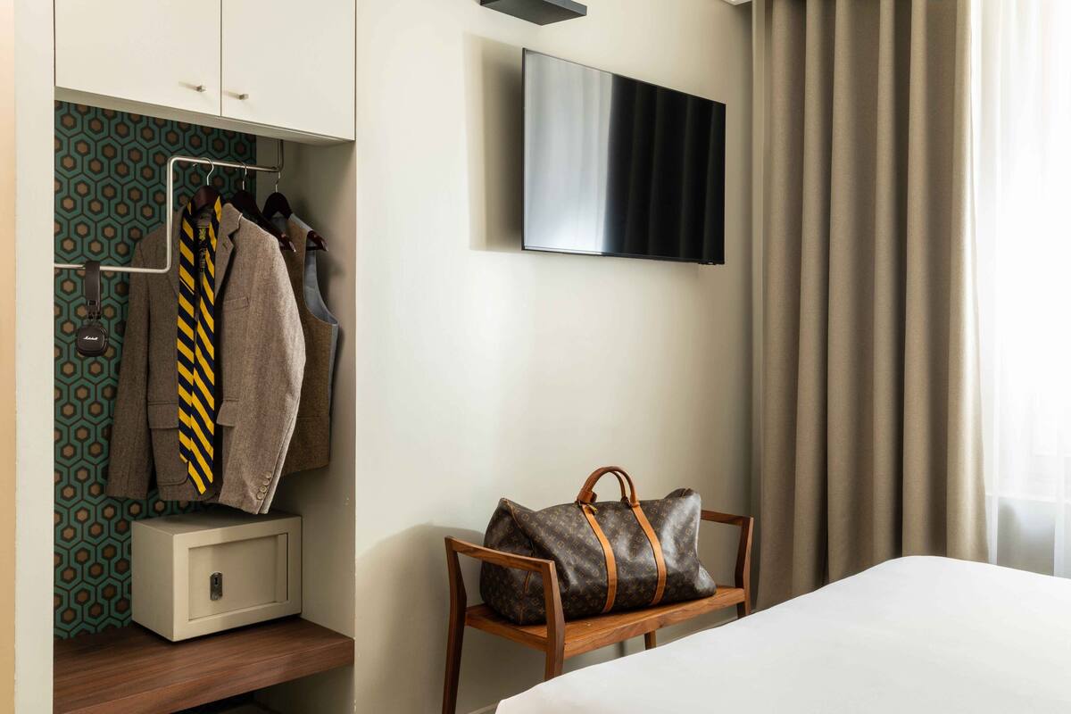 A hotel room with a wardrobe, a bed, a television, and a chair.