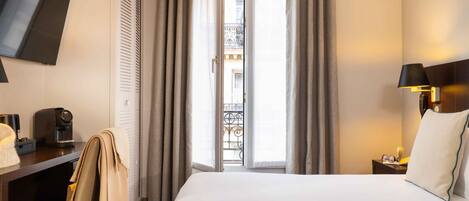 Habitación de hotel con cama, escritorio con cafetera, silla y televisor montado en la pared.