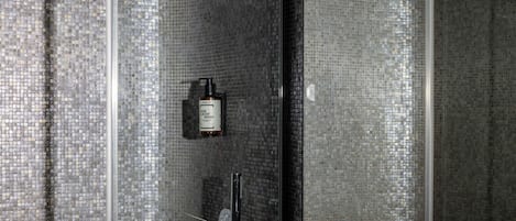 A bathroom with a shower, a bottle of hair and body wash, and a glass rack with glasses.